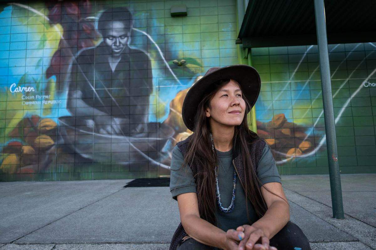 Artist Mari Shibuya sits near her completed mural of Carmen Mueses, a cocoa farmer in the Dominican Republic, located at Central Co-op, 4502 N. Pearl St. in Tacoma, Wash. The project was commissioned by Fairtrade America as part of its “Choose the world you want” public art campaign.
