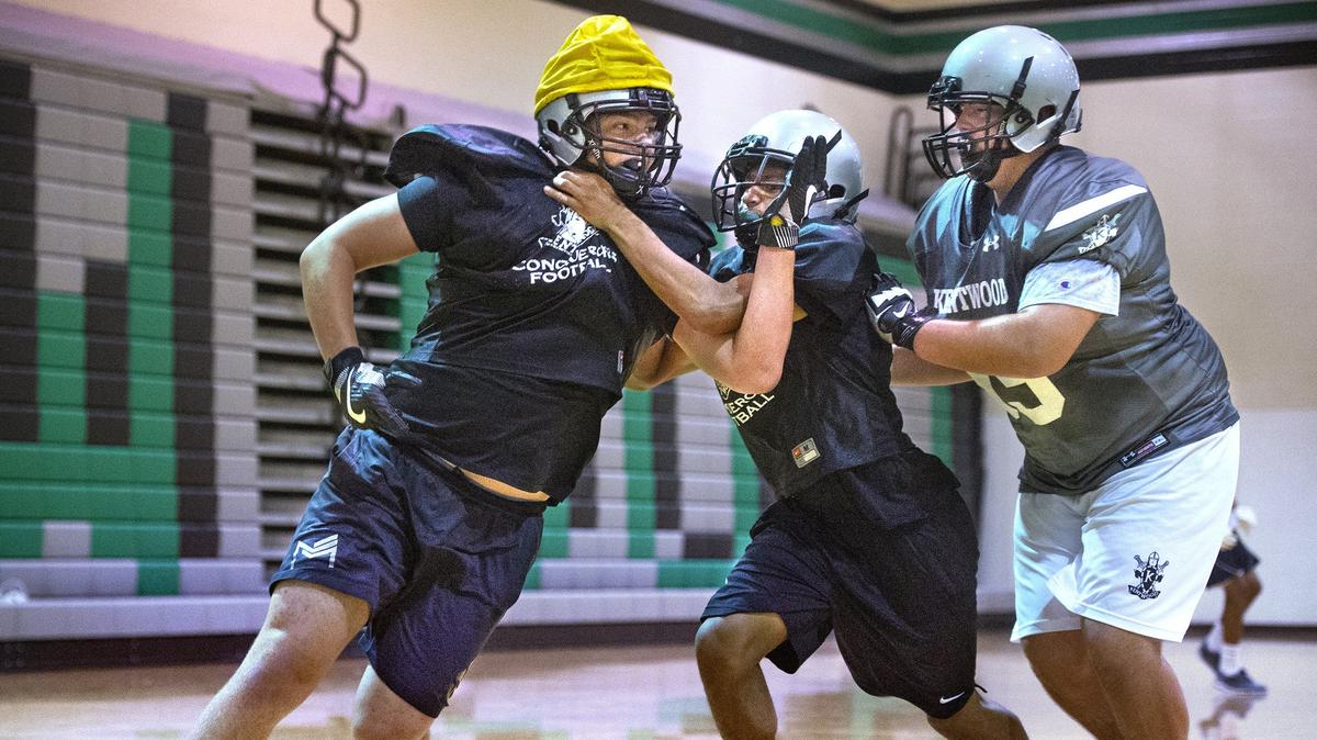 Kentwood junior lineman Wyatt Hansen (left) powers around double team blocking during preseason football practice at Kentwood High School in Covington on Wednesday, Aug. 22, 2018.
