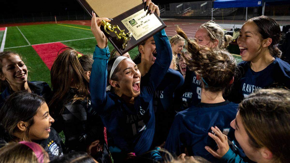 Auburn Riverside forward Samiah Shell hoists the 3A West Central/Southwest bidistrict championship trophy while surrounded by teammates after the Ravens beat Peninsula, 2-0, on Thursday, Nov. 3, 2022, at Mount Tahoma High School in Tacoma, Wash.