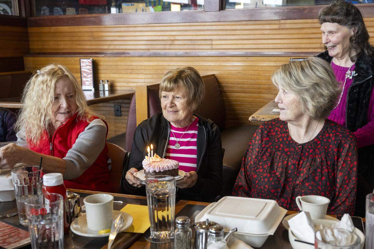 Sue Newman, center, receives a birthday cake after the group has eaten on Thursday, Feb. 19, 2026, in Tacoma, Wash. On the third Thursday of every month, lunch with the Bon crew includes birthday cakes, gifts and cards for members born that month.