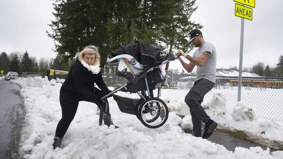 Principal Mandy Jessee helps parent Romeo Rodriguez negotiate his stroller over deep snow outside Tumwater Hill Elementary School on Friday, Feb. 15, 2019. “I thought it was cleared,” Rodriguez said after running into more than a foot of snow, slush and ice blocking the sidewalk after walking his second-grade daughter, Leticea, to school.