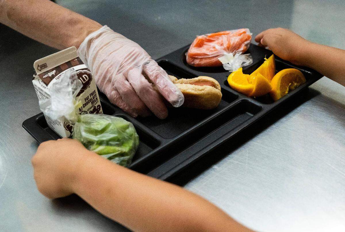 Evergreen Elementary cafeteria staff member Heather Thomas places a hotdog on a student’s lunch tray as they pass through the lunch line at Evergreen Elementary in Spanaway on Friday, June 10, 2022.
