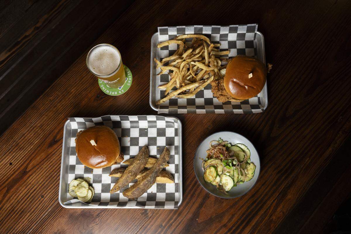 Two Barn Burner fried chicken sandwiches, served with jos, bottom left, and hand-cut fries, top right, are pictured with a cucumber salad with sesame vinaigrette, bottom right, on Wednesday, Jan. 7, 2026, at Terry's Bar and Grill in Tacoma, Wash.