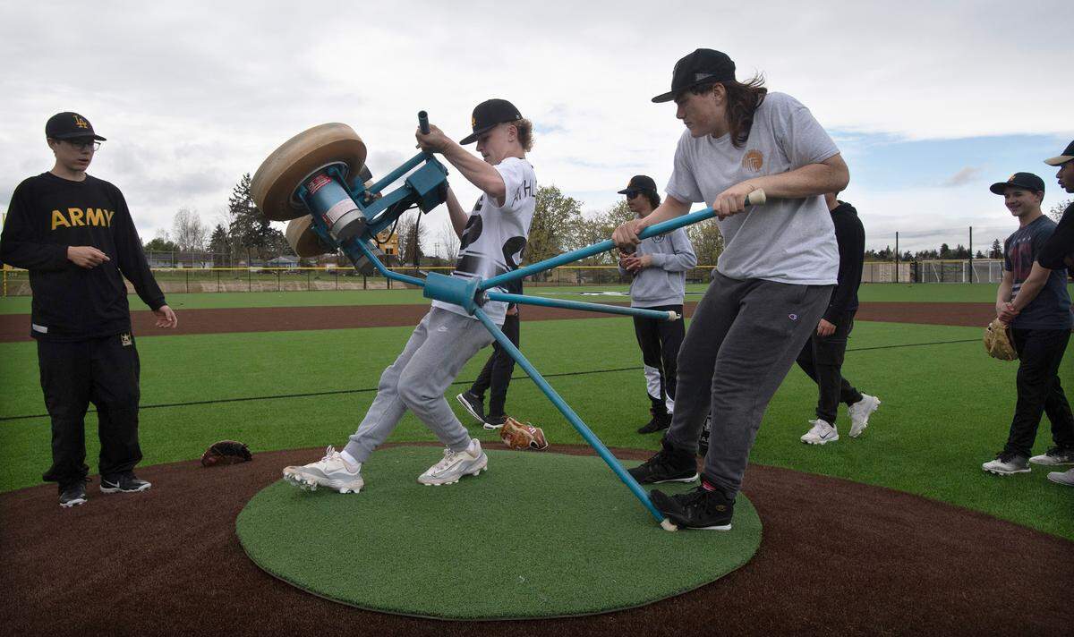 Lincoln baseball players set up a pitching machine for practice on the new turf field at Lincoln High School in Tacoma, Washington, on Monday, April 8, 2024.