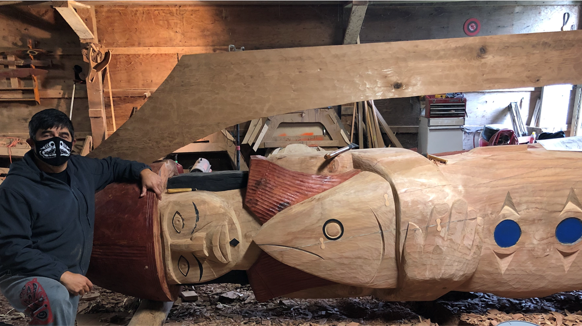 Artist Guy Capoeman poses with his partially finished sculpture, “Our Fisherman, Our Guardian,” in his Quinault Nation workshop.
