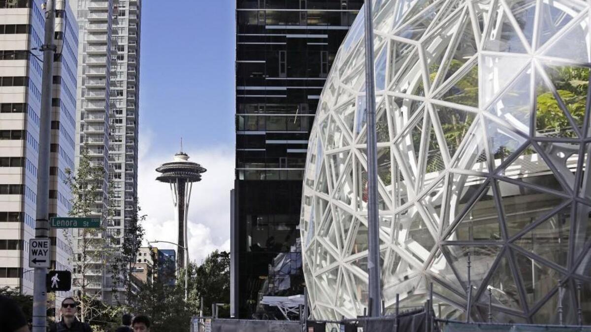 In this Wednesday, Oct. 11, 2017, photo, large spheres take shape in front of an existing Amazon building and in view of the Space Needle in Seattle. A huge spike in housing prices, traffic snarling downtown, long-time residents and businesses displaced. The dozens of North American cities vying to become Amazon’s second home are focused on the positives of luring the tech giant. But many in Seattle say Amazon’s explosive growth has not been without a significant downside in its birthplace. (AP Photo/Elaine Thompson)