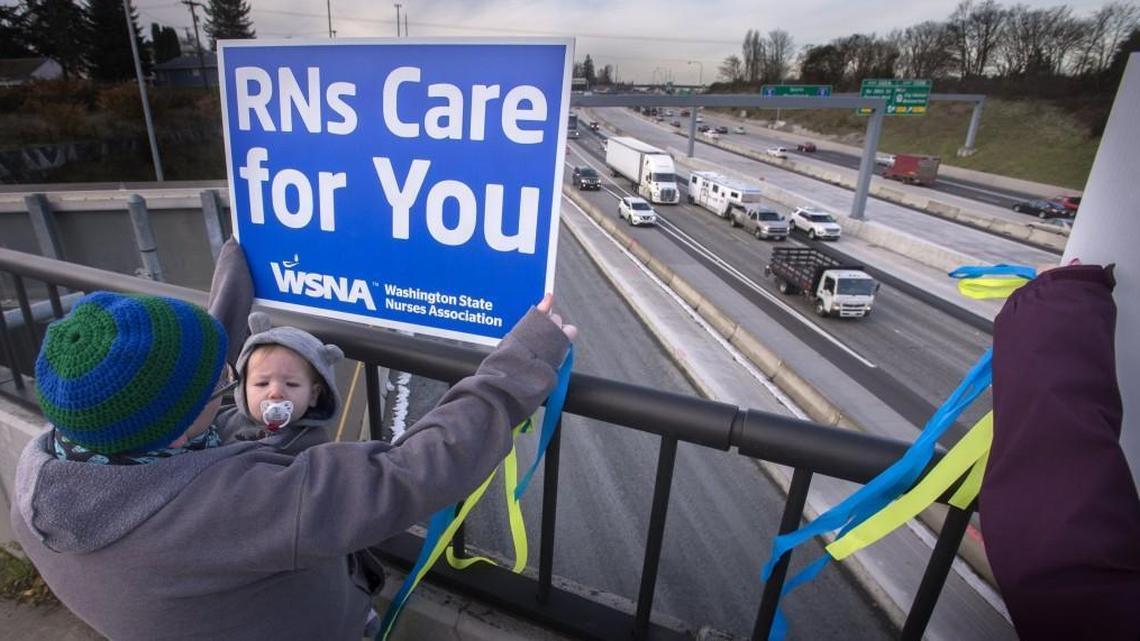 Erin Morrison, a nurse at Tacoma General Hospital, holds a sign up for passing drivers while keeping her 11-month-old son, Ira, warm under her jacket during a rally on the Yakima Avenue overpass over Interstate 5 in Tacoma on Wednesday. The nurses’ rally comes before taking an advisory strike vote against Tacoma General on Friday.