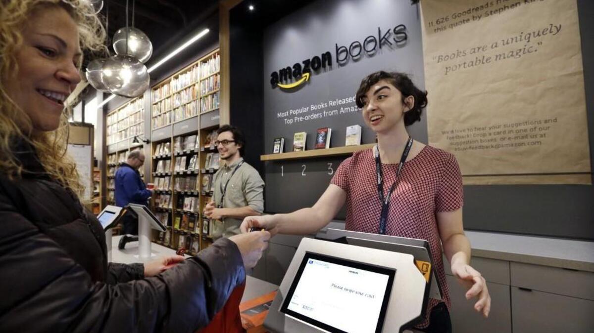 Customer Kirsty Carey, left, gets ready to swipe her credit card for clerk Marissa Pacchiarotti, as she makes one of the first purchases at the opening day for Amazon Books, the first brick-and-mortar retail store for online retail giant Amazon, Tuesday, Nov. 3, 2015, in Seattle. The company says the Seattle store, coming two decades after it began selling books over the Internet, will be a physical extension of its website, combining the benefits of online and traditional book shopping. Prices at the store will be the same as books sold online.