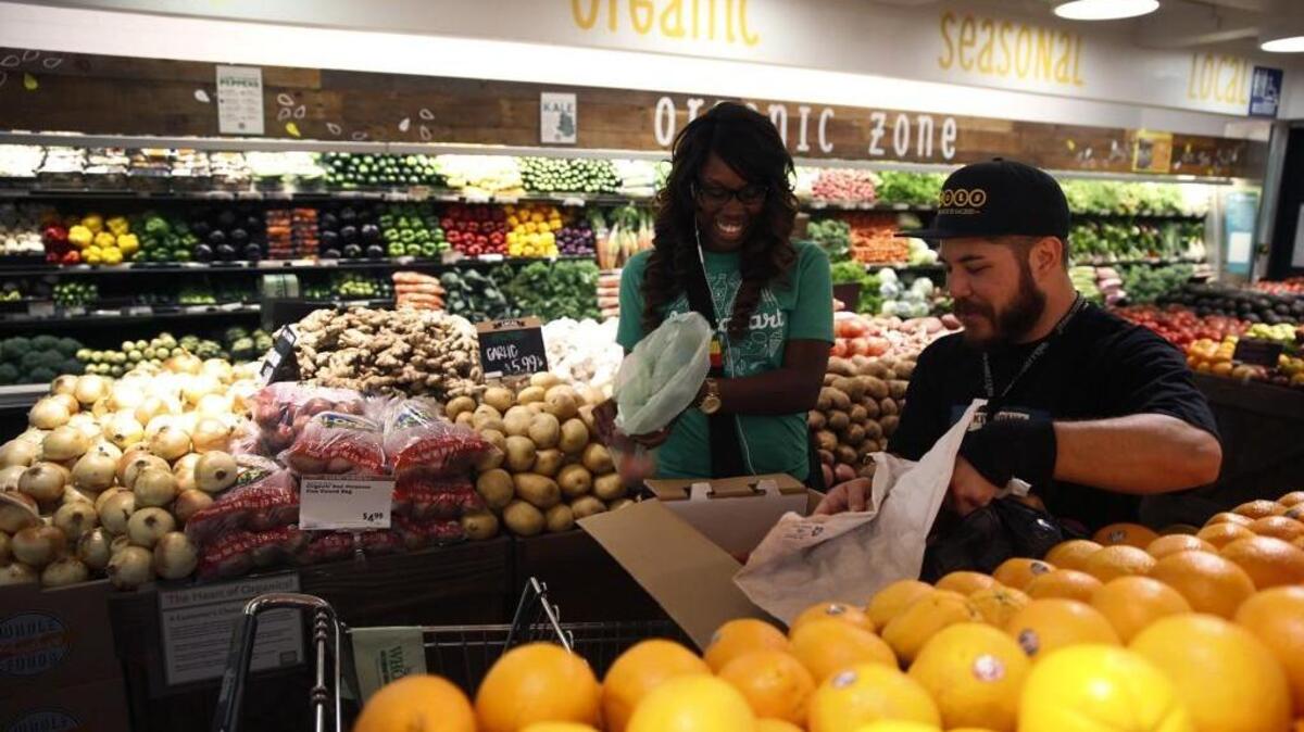 Whole Foods team member Matthew Otsuka opens a box of peaches for Instacart shopper Kara Pete as she shops for a customer in Sherman Oaks, Calif. Instacart is expanding its shopping/delivery zone in the South Sound area later this week.