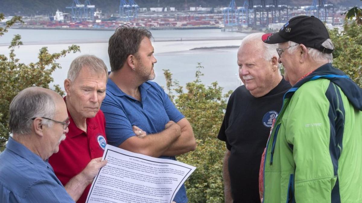 Bronze artist Paul Michaels, left, reads Thursday from a paper proof of the bronze plaque that will be installed on the Murray Morgan Bridge to commemorate the bloody 1916 Longshore strike. Listening to Michaels are, from left, Mike Jagielski, president of Tacoma Pensioners; Dean McGrath, president of ILWU, Local 23 Tacoma; James Norton, pensioner; and Ronald Magden, Local 23 honoree member.
