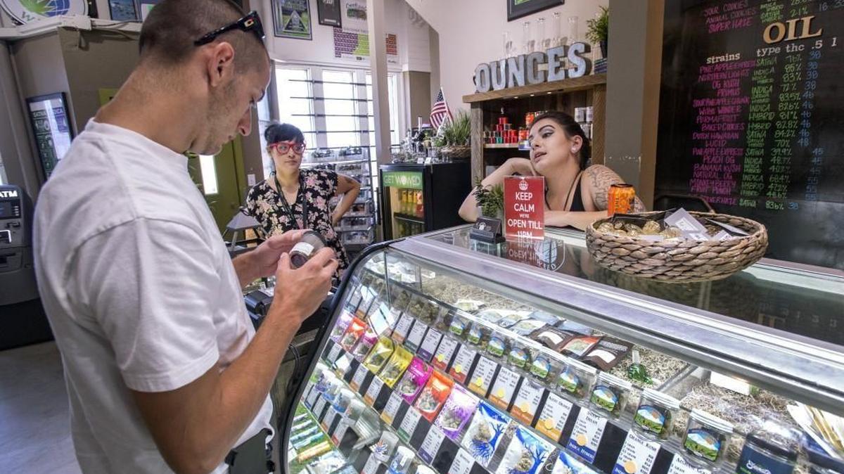 Customer Josh Reed contemplates a marijuana purchase in Tacoma as World of Weed employees Emily Howell, right, and Kayla Beck look on in August. Pot sales and their taxes are hot on the heels of hard alcohol, based on an analysis of purchase and tax records from two state agencies.