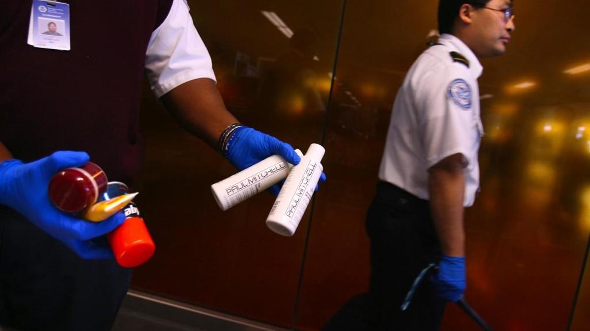 A6, 09/10/2006; TSA screening officer Calvin Chin walks past a fellow officer taking liquid and aerosol hair products from a passenger at the security area at SeaTac airport on Tuesday morning.