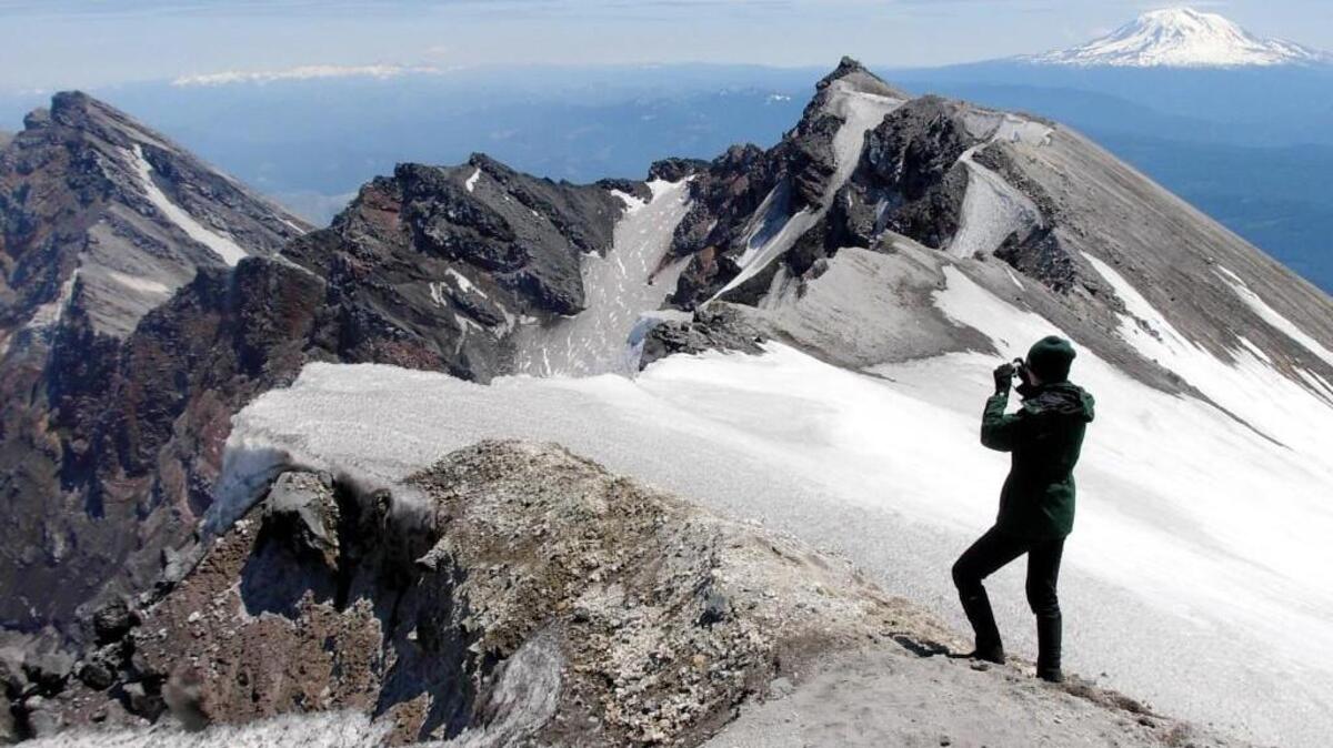 Climbing Ranger Gretchen Schwinn looks out over the crater rim of Mount St. Helens on Tuesday, June 12, 2007 with Mount Adams in the distance.