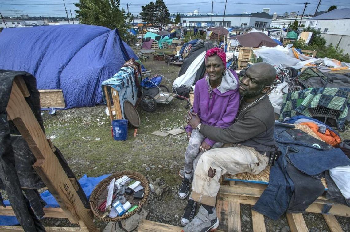 William “New York” Bell hugs his partner Ulonda Berry Bell Friday as the city of Tacoma worked to provided temporary washing stations, restrooms and and waste bins to improve health and sanitary conditions in the camp that serves as home to over 50 people. The couple said that they appreciated the city’s effort to make conditions more livable but said what they needed was a real home off the streets.