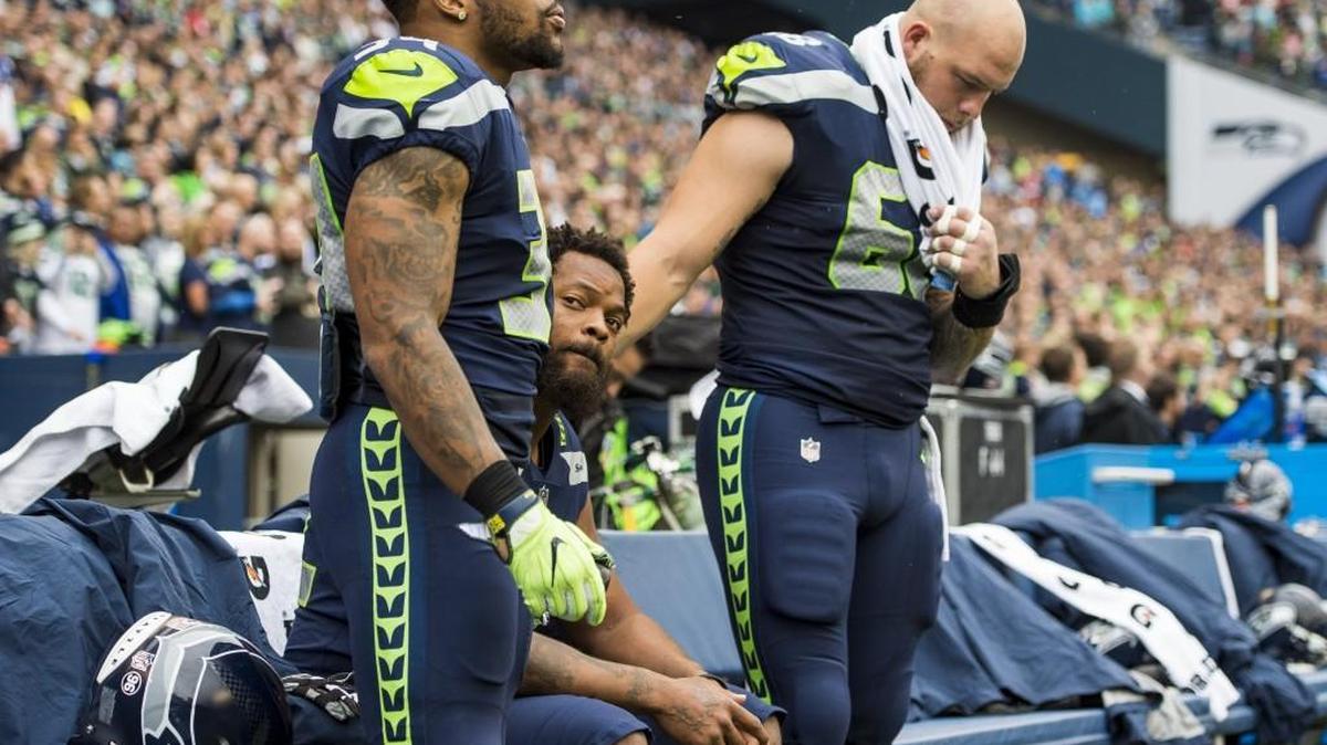 Seahawks running back Thomas Rawls and Seahawks offensive lineman Justin Britt stand with Seahawks defensive lineman Michael Bennett as he sits during the national anthem. The Seattle Seahawks played the San Francisco 49ers in Seattle's home opener at CenturyLink Field in Seattle, Wash., on Sunday, Sept. 17, 2017.