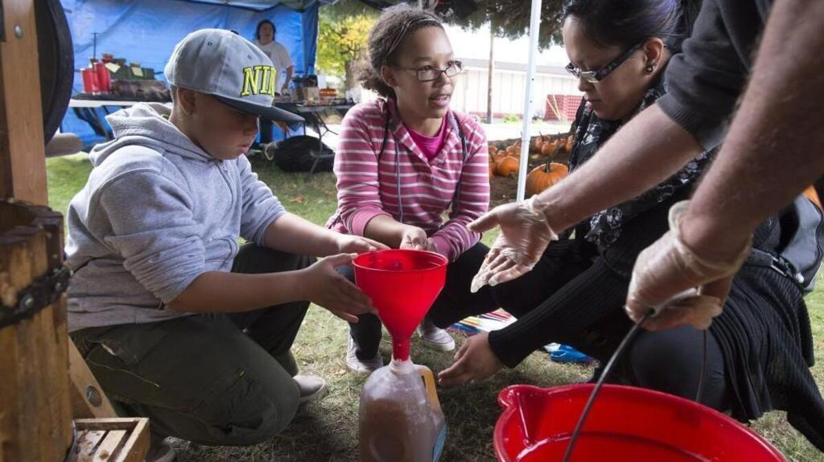 
Elizabeth Custodio, right, and her children, Timothy, 9, and Taylor Babbel, 12, fill a jug with cider at the Meeker Mansion Cider Squeeze in Puyallup Saturday.
