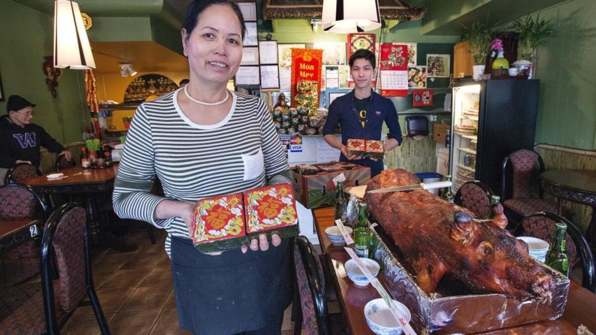 Many Vietnamese prepare for the Lunar New Year by cooking special holiday foods, such as these banh chung displayed by Xuan Phan, owner of the Pho Dragon restaurant, and manager Tan Nguyen. The delicacy, essentially sticky rice with vegetables or meat filling cooked in banana leaves, are similar to tamales. The whole roast pork at right is part of a larger offering to bring the restaurant good luck and to honor their ancestors.