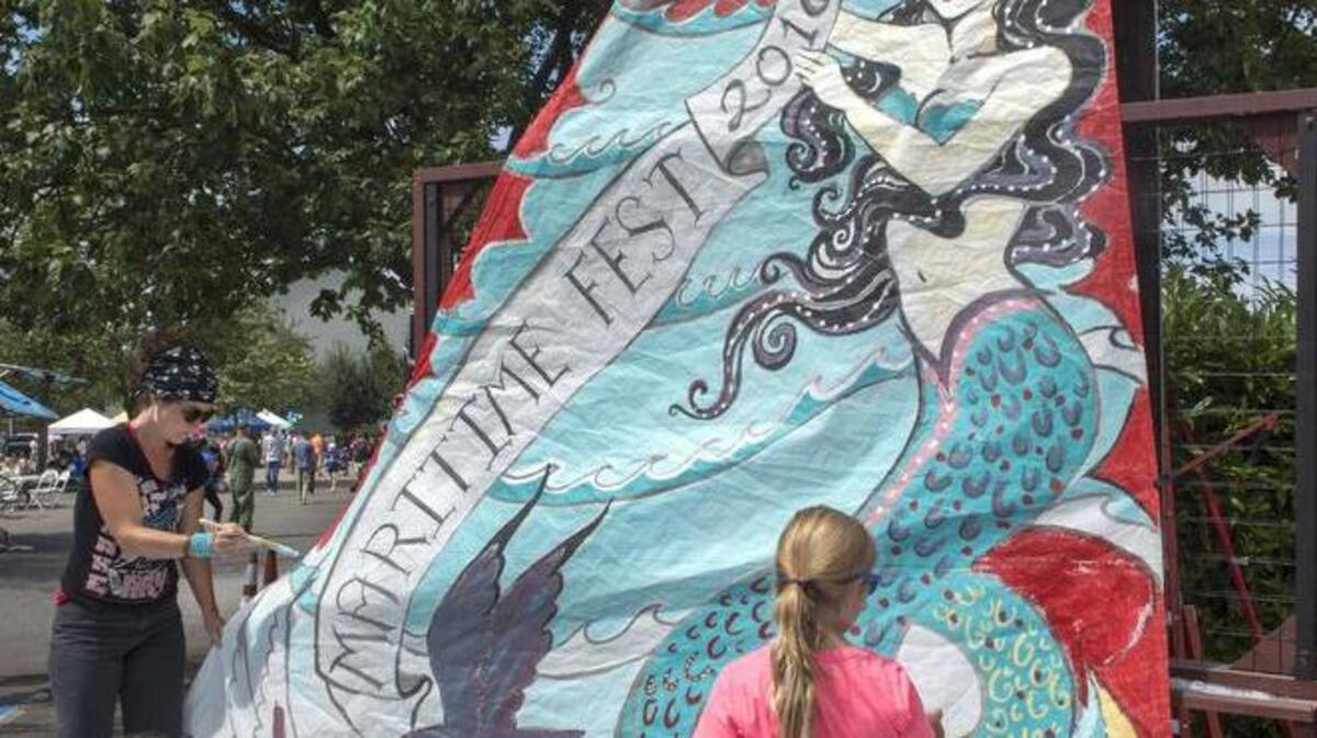 Two young volunteers help artist Glory Cancro paint a sail Saturday that she designed for Maritime Fest.