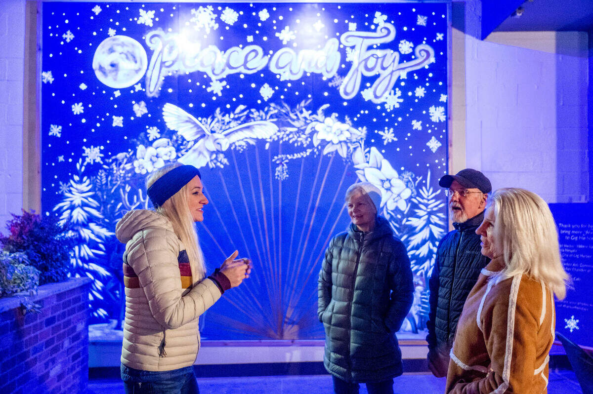 Hillarie Isackson, an artist from Gig Harbor, talks to Liz Miser (center-left), her husband, David, and Liz’s sister Joan Warrington, after they took a photo in front of her “ultraviolet active” mural of Sunday night along Harborview Drive in Gig Harbor.