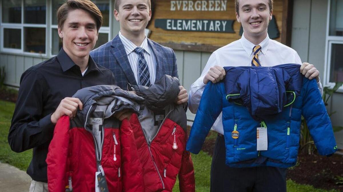 Austin Mallavia, Dacre Folden and Anthony Lusk, from left, hold up jackets in front of Evergreen Elementary School on the Key Peninsula. Foden is working with the nonprofit Charlie’s Dinosaur at Evergreen Elementary and will hand out jackets to kids in need.