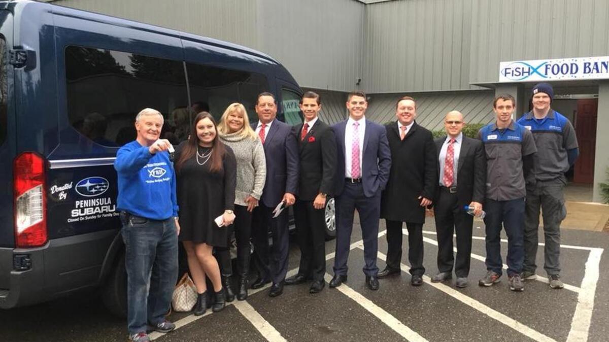 Gig Harbor Peninsula FISH Food Bank director Ron Coen, left, holds up the keys to the new 2017 Ford Transport van donated by Peninsula Subaru owner John Dionas, fourth from left, during a ceremony Friday at the nonprofit’s headquarters in Gig Harbor. Dionas was joined by his family and staff members from the dealership.