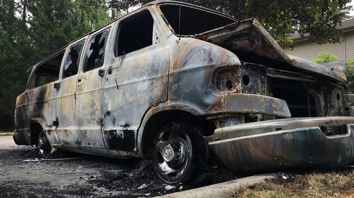 A burned 1999 Dodge Ram van sits in the parking lot of Fox Island Alliance Church in Fox Island on Monday. The van belonged to an intern group from Youth With a Mission, an inter-denominational, nonprofit Christian missionary organization.