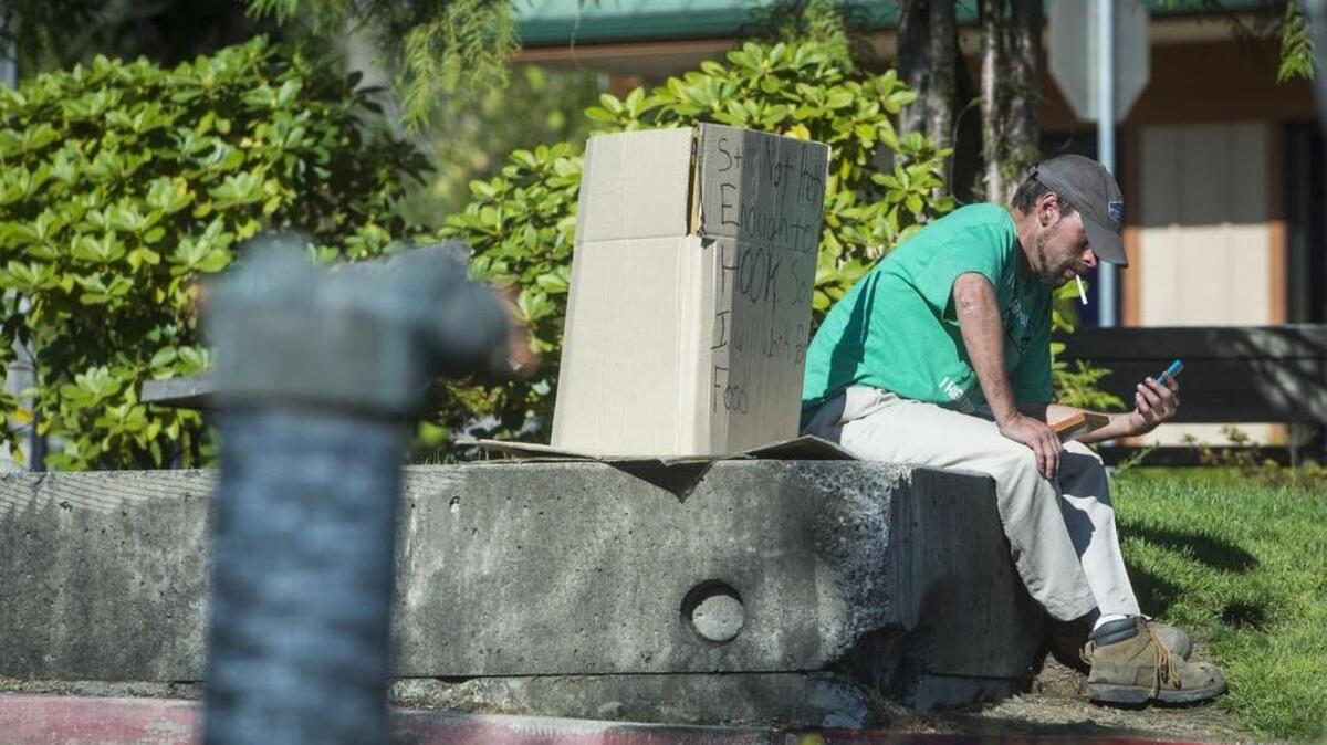 A man sits next to a sign offering to work for food outside of McDonald’s in Gig Harbor on Aug. 20.