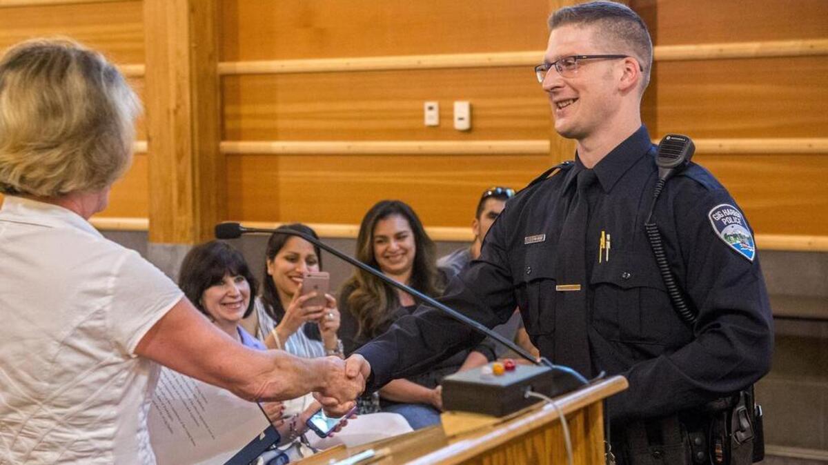 New Gig Harbor police officer Patrick Sam shakes the hand of Mayor Jill Guernsey after she administered his oath at Monday’s City Council meeting. Behind is his wife, Louisse, left, and friends.