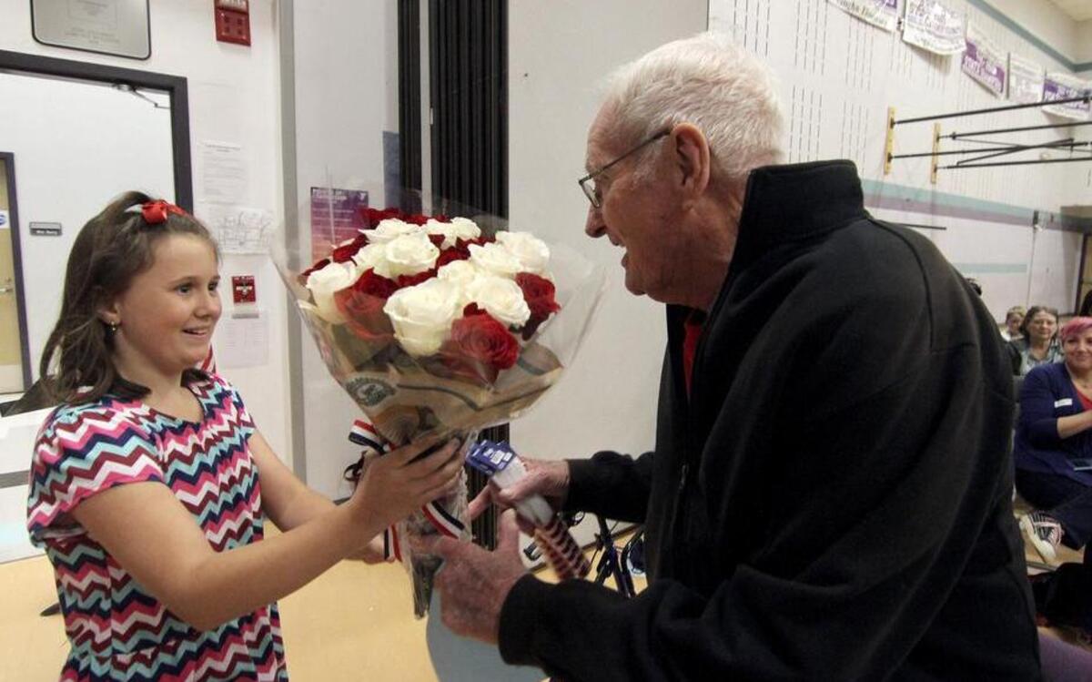 Vaughn Elementary School student Ali Kimball presents former U.S. Navy veteran and new friend William Deller with flowers as an honor to his World War II service during Tuesday’s assembly at the school. The two formed a relationship through letter-writing program at the school.
