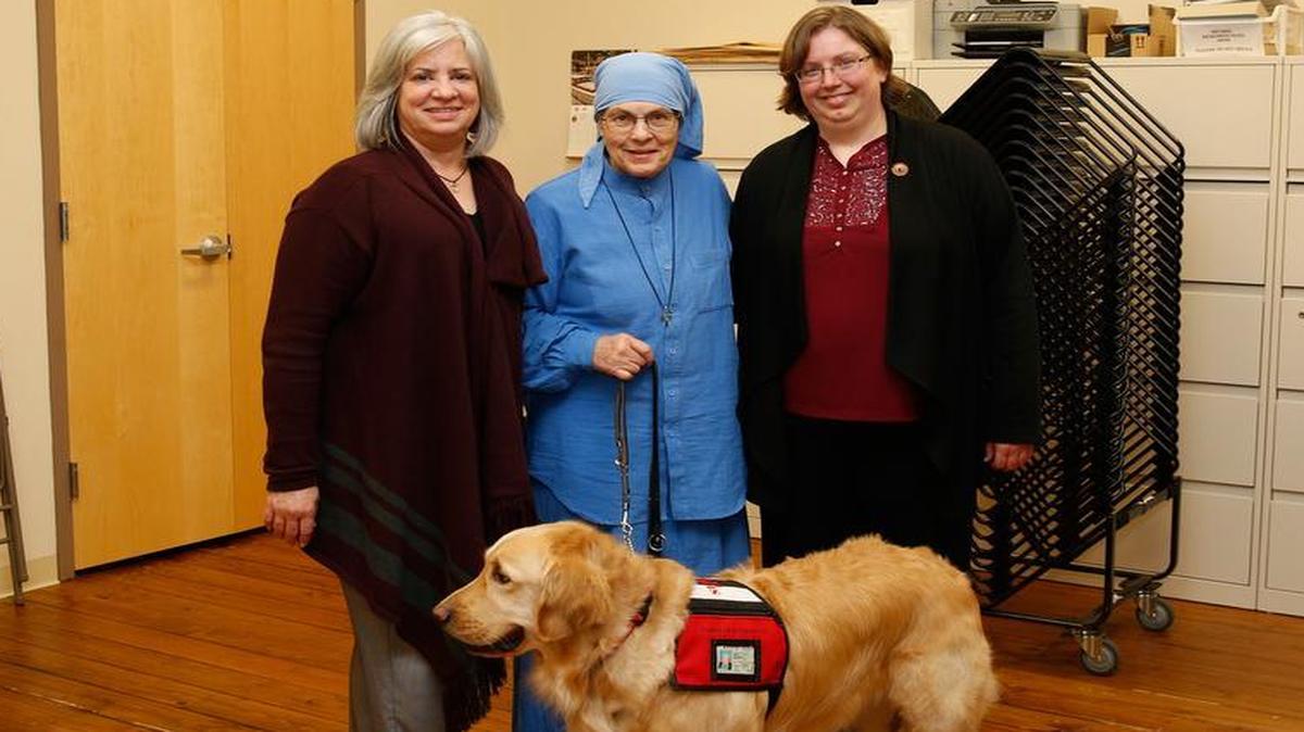 Prison Pet Partnership executive director Beth Rivard, Sister Pauline Quinn, who founded the program, and Service Dog Program manager Grace Van Dyke, from left, gather with Pax, a golden retriever, during a meeting about the program April 13 in Gig Harbor.