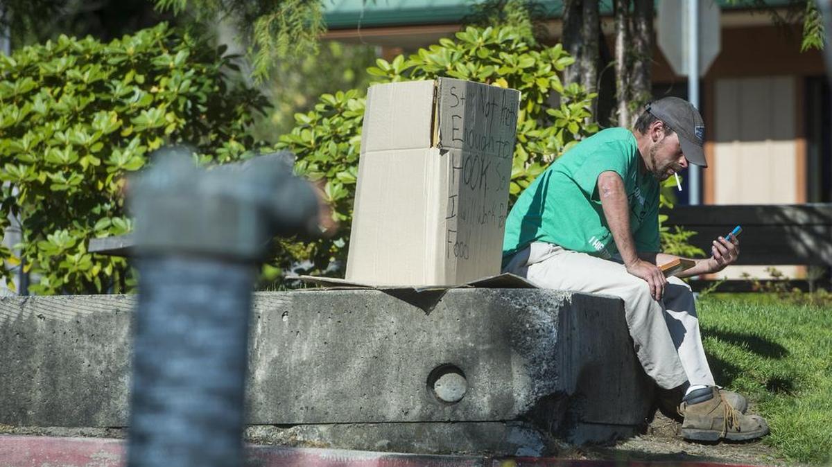 A man sits next to a sign offering to work for food outside of McDonalds in Gig Harbor on Sunday, Aug. 20.