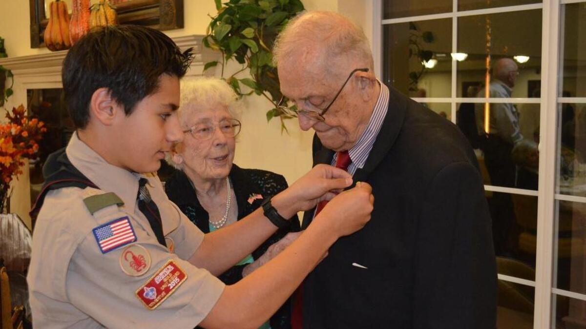 Boy Scout Troop 27 Scout Reece Zusy pins a badge of honor on World War II veteran Ordean Helland as fellow resident Lois Martin observes during a Veterans Day ceremony Friday at Peninsula Retirement home.