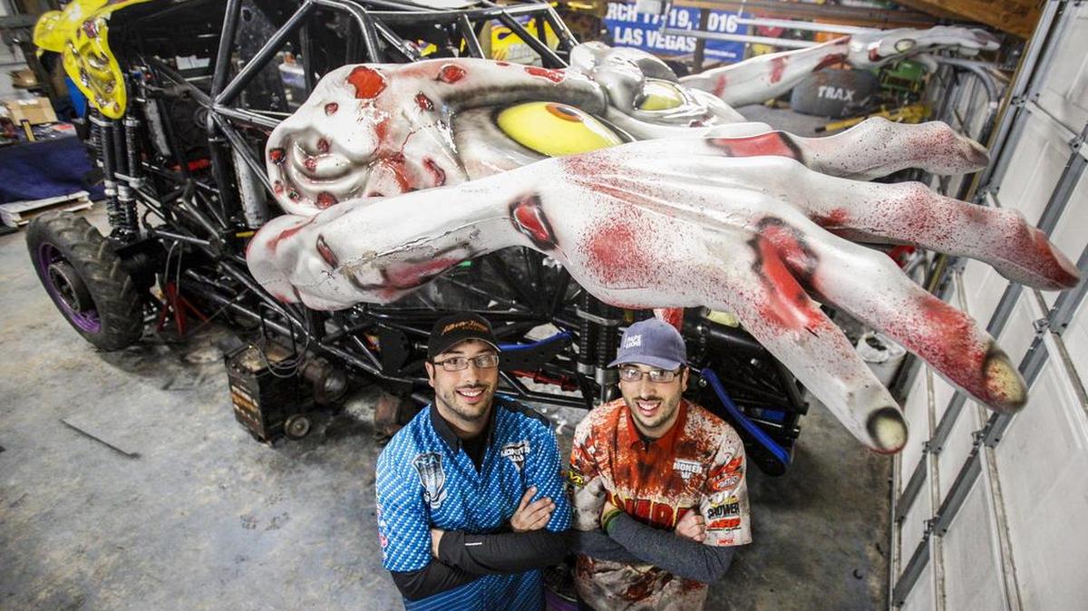 Identical twins Travis, left, and Tyler Groth stand under “Zombie,” Tyler’s monster truck, at the brothers’ workshop in Port Orchard. Both brothers will participate in this weekend’s Monster Jam Triple Threat Series presented by AMSOIL, which takes place at the Tacoma Dome.