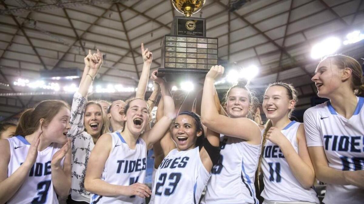 The Gig Harbor Tides hoist the state championship trophy following their 51-48 victory over Garfield in Saturday night’s 3A girls basketball state title game in the Tacoma Dome.