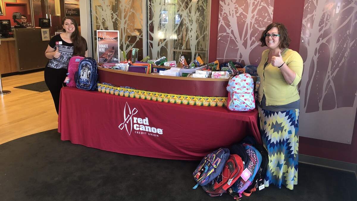 Red Canoe Credit Union staff members Carissa Crawford and Chantel Bowers stand beside a canoe full of school supplies. The school supply drive supports Puyallup School District students who can’t afford their own materials.