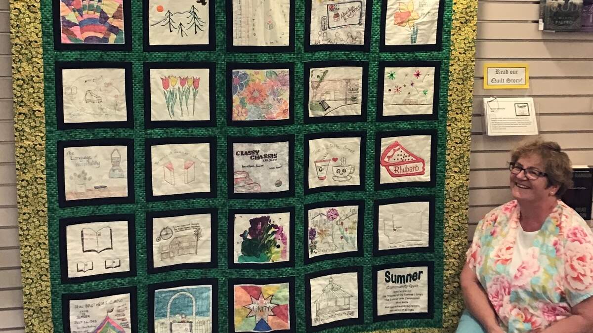 Anita Sheneberger, a former librarian for the Sumner Pierce County Library, sits beside a community quilt she put together. The quilt was created by a total of 30 people who live and work in Sumner and is meant to travel around places in the city.