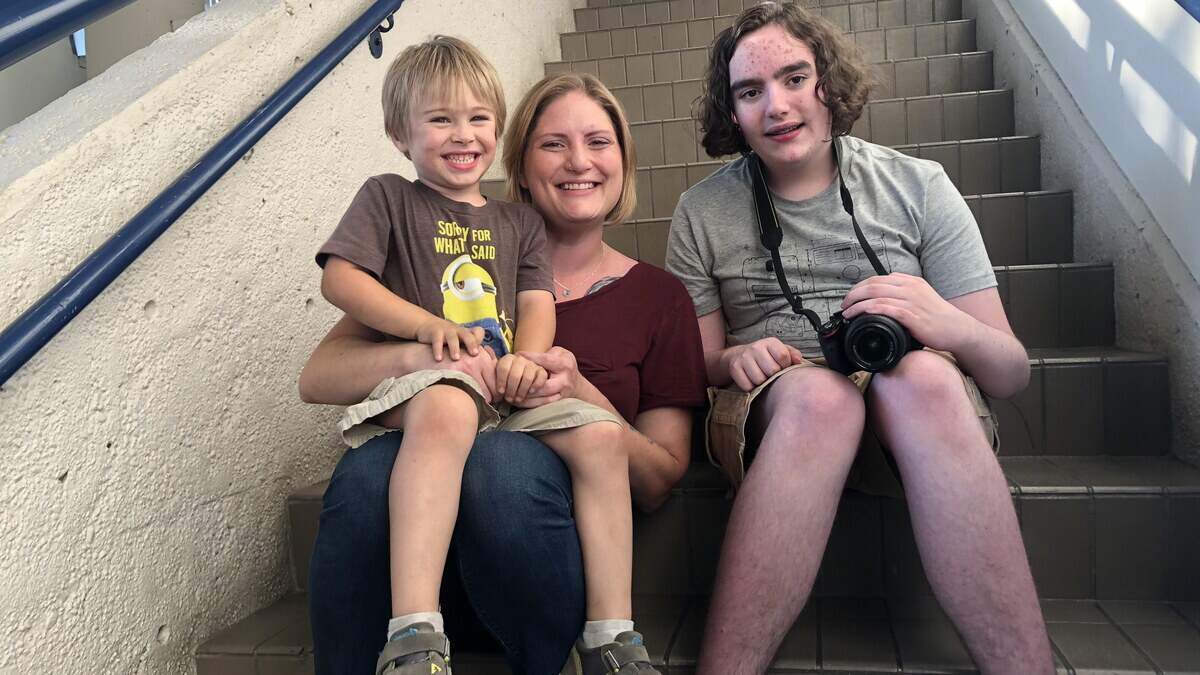 From left: Garvan MacFarlane, Crystal Kennedy and Mike Williams sit together outside the art exhibit at the Washington State Fair. MacFarlane and Williams participate in Special Portraits Exceptional Photography Club, a club for kids with disabilities run by Kennedy. Sept. 6, 2018