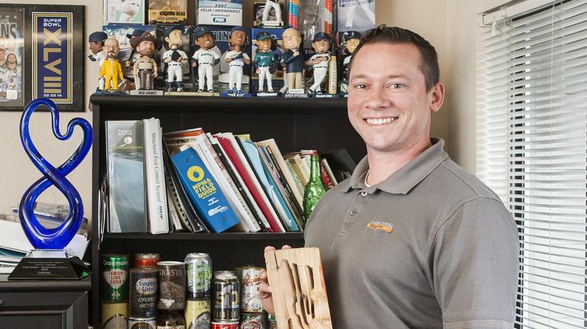 Luke Rambo stands with a piece of wood showing carpenter ant damage alongside Young Entrepreneur of the Year Award at his office on South Hill. Rambo won a Young Entrepreneur of the Year Award at PestWworld 2016 in Seattle with his business, Rambo Total Pest Control.