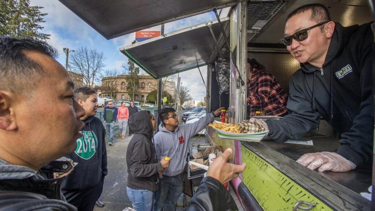 Scott Valen, right, serves up a burger and fries from Stacks, one of the two food trucks which greeted dozens of customers at the new food truck lot in Tacoma earlier this year. The Puyallup City Council is considering a pilot program would allow food trucks to locate on public street parking.