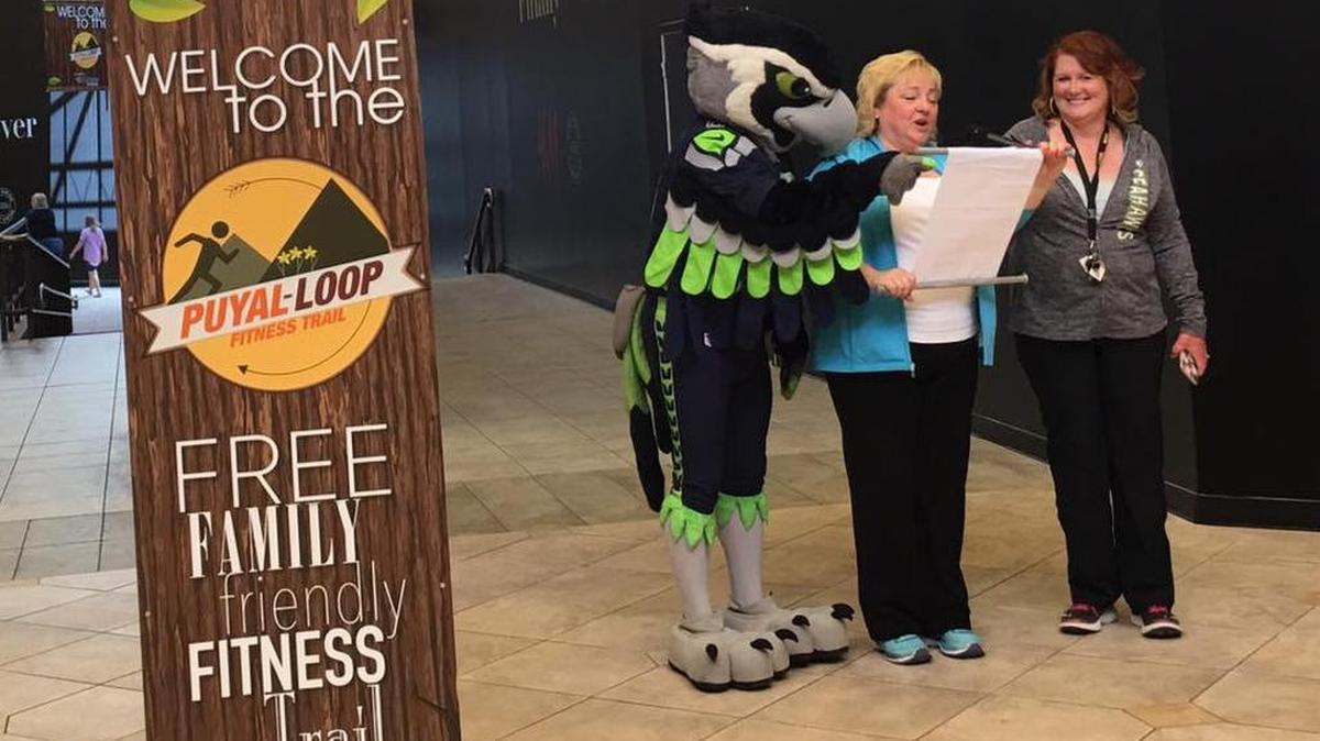Seattle Seahawks mascot Blitz helps Shelly Schlumph, Puyallup/Sumner Chamber of Commerce president and CEO, center, and Patty Summers, South Hill Mall marketing director, celebrate the opening of the mall’s new indoor fitness trail, the Puyal-LOOP, during a ribbon-cutting event July 22.