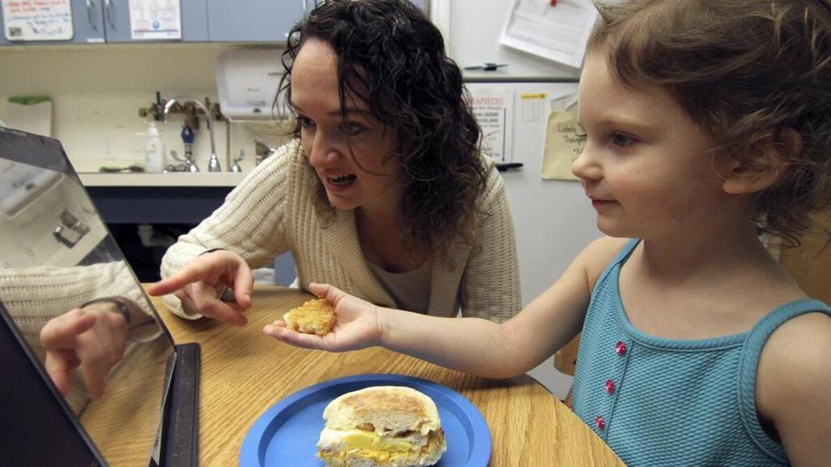 Good Samaritan Hospital Children’s Therapy Unit speech therapist Jessica Clark works with 3-year-old patient Kelsey Yates of Auburn last week. Clark shows through Yates’ image in a mirror how to properly chew her food to help her overcome her reluctance to eat. It’s a part of the big-picture treatment plan to help the young girl who at birth had extra cartilage that partially obstructed her epiglottis from closing correctly.