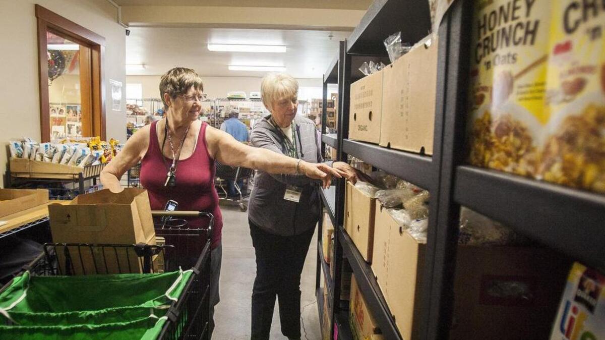 Ruth Cole, left, grabs bagged grains while helped through the food bank by Ann Yost, volunteer and supervisor, at the FISH Food Bank in Edgewood last week.