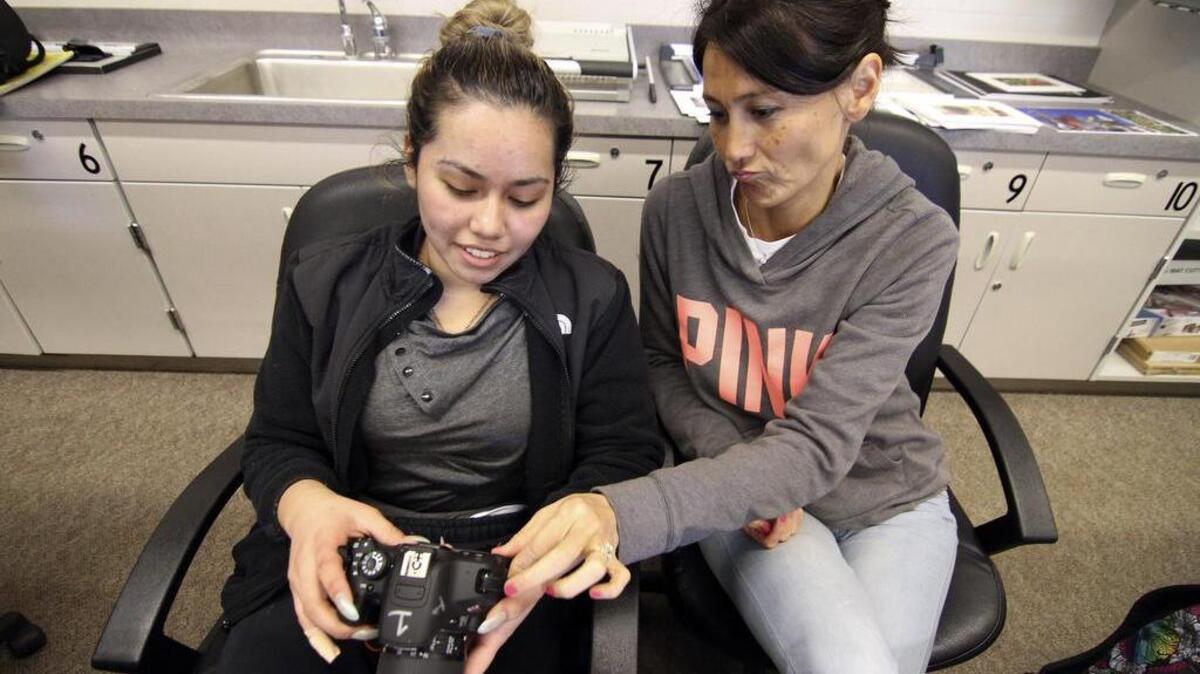Rogers High School photography teacher and yearbook advisor Pam Sarell helps student Brianna Armenta with a digital camera in class last week.