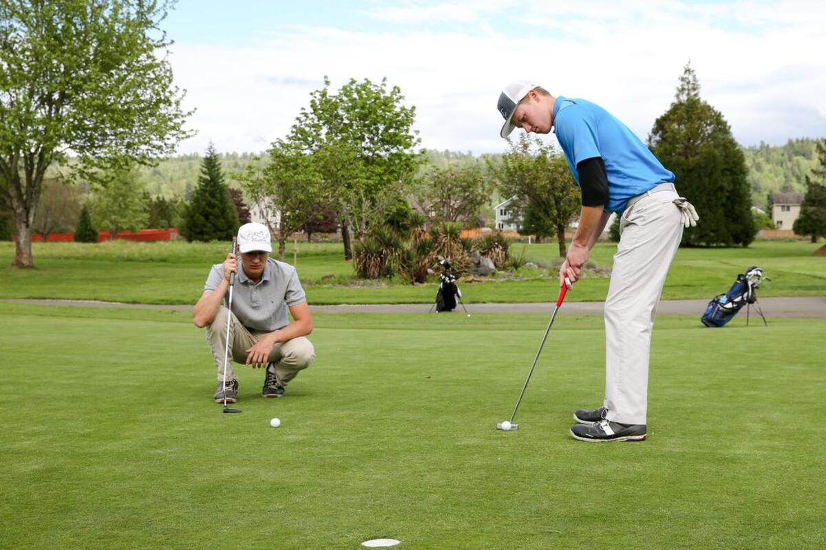 Cascade Christian High senior Nathan Beardemphl, left, helps teammate Dylan Gritter lineup his putt on the green at Hole 1 during a practice round last week at High Cedars Golf Course in Orting.