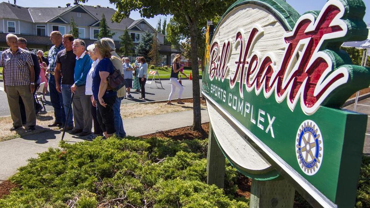 Bill Heath, in the center holding a cane, stands with other members of the Sumner Rotary Club and community members for a photo in front of a new sign during a ceremony renaming the Daffodil Valley Sports Complex the Bill Heath Sports Complex in Sumner on Aug. 16.