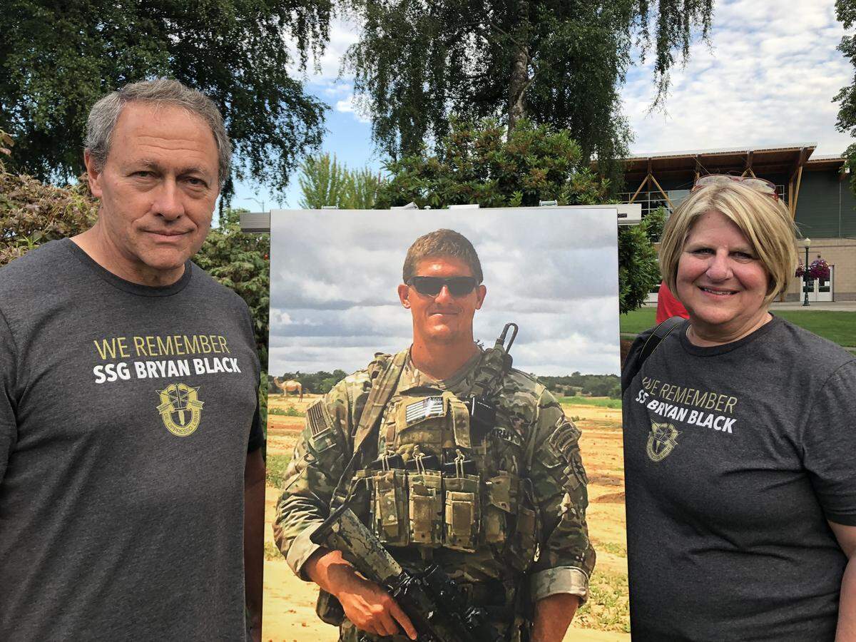 Hank Black, left, and Karen Black stand beside a photo of their son, Staff Sgt. Bryan Black, who died while serving last year. Bryan was remembered with a chess table memorial on July 5, 2018.