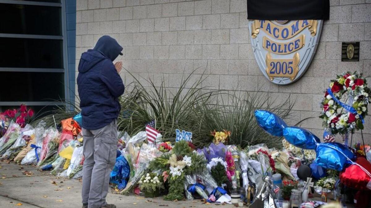 A citizen pays respect with a prayer for fallen Tacoma Police officer Jake Gutierrez at a memorial with flowers in front of the Tacoma Police headquarters on Thursday, Dec. 8, 2016.