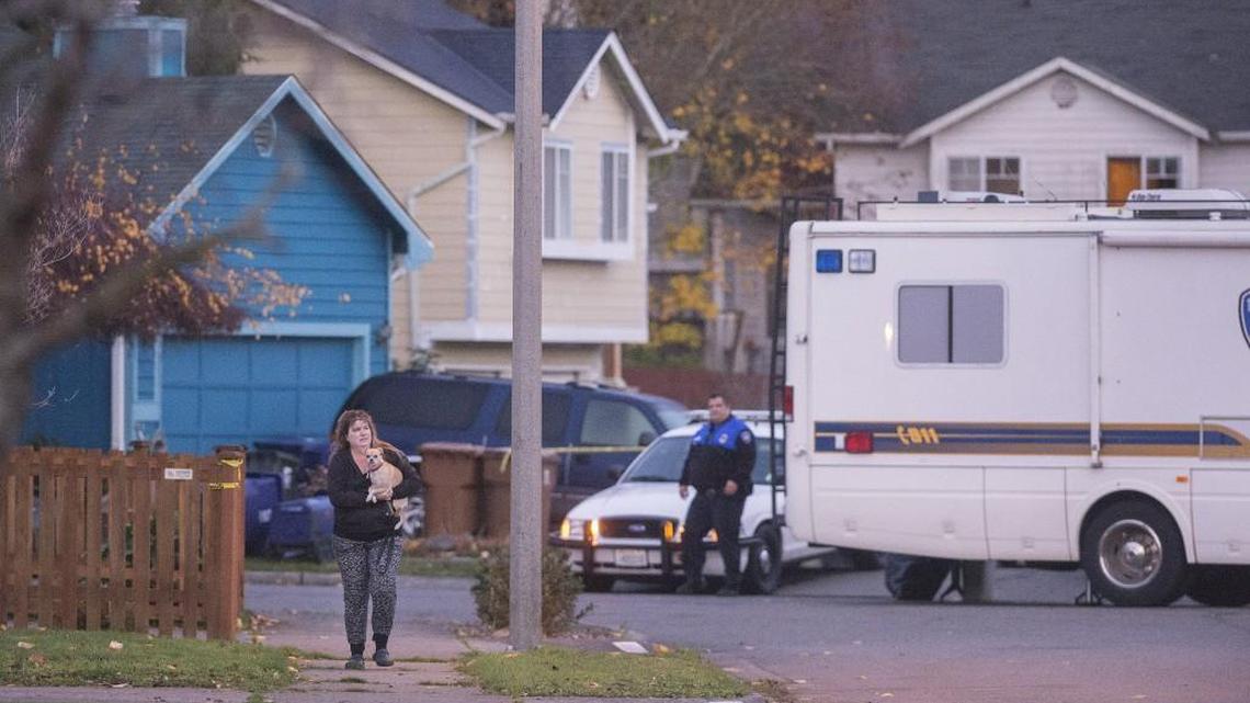 A resident holds her dog close Thursday morning after speaking with an officer near the house, far right, where the suspect was shot and killed.