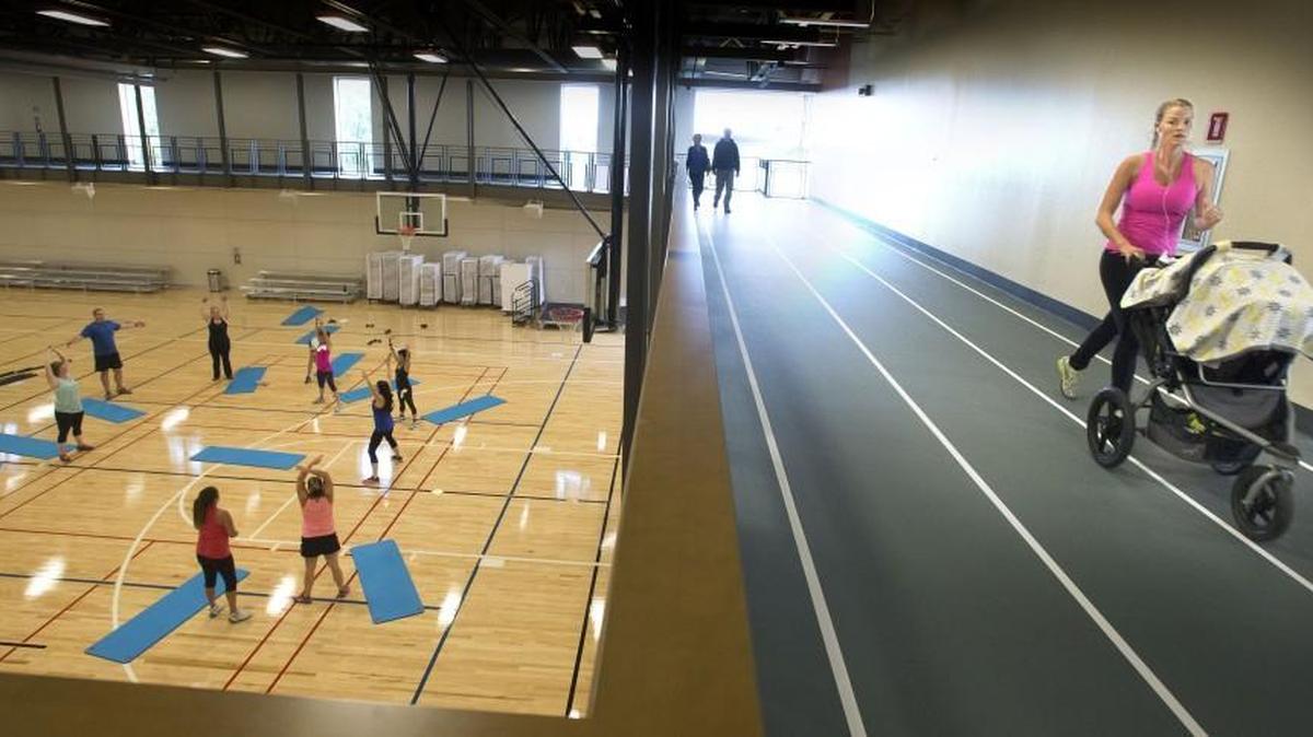 
Shelby Barkshire, right, pushes her son, Easton, 2 months, in a stroller while jogging on the second floor track, as a class stretches out on the first floor at the new Gordon Family YMCA in Sumner on Monday. Seven laps around the track equals one mile at the largest YMCA in the state.
