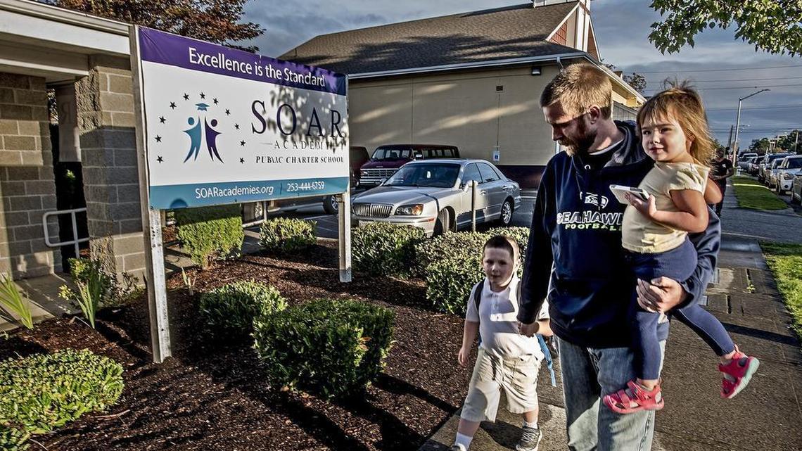 Greg Allman, carrying 2-year-old daughter Genevieve, walks in May 2014 with his son Liam, 5, to the SOAR Academy, one of three charter schools that opened this year in Tacoma. The school says it is looking into forming an affiliation with a public school in the state to remain open.